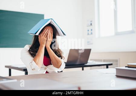 Tired female student sitting at the table with a book on her head. Stock Photo