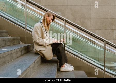 Young beautiful happy smiling business lady working with laptop, while sitting on the stairs outdoors Stock Photo