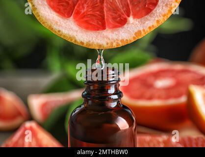 Citrus essential oil dripping from grapefruit slice into bottle, closeup Stock Photo