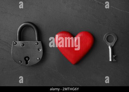 Padlock, wooden heart and key on black stone background, flat lay. Relationship problems concept Stock Photo