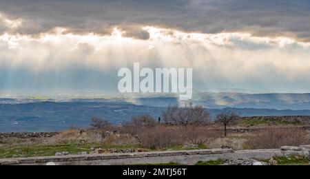 Groups of sunburst rays burst through the Turkey dark clouds lighting up patches of hillside greenery Stock Photo