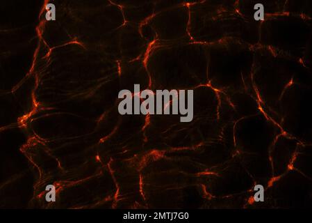Photos of the texture of the reflection of light from the transparent surface of the water and the waves in bright red tones. Abstraction. Stock Photo