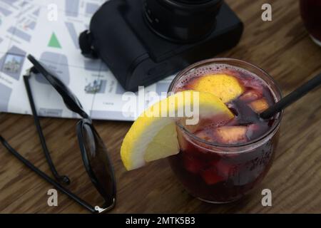 View from above of a table where a tourist is having a glass of sangria with lemon, next to a map and a camera Stock Photo