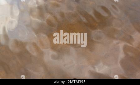 Photo of the reflection of light from the surface of the movement of the water waves of the river from the sky in light orange tones. Abstraction back Stock Photo