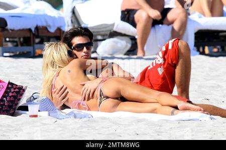 Wearing a camouflage bikini with pink trim, Former Playboy Playmate Shauna Sand spends a romantic day on the beach with her new husband Laurent. She proudly displayed her new ring, covering the ring tattoo she had from her previous marriage, and the two lovebirds strolled together on the beach. Shauna took some time to give Laurent a back massage and the two lovingly kissed while they relaxed on the sand. Miami Beach, FL. 2/21/11. Stock Photo