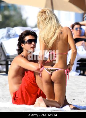 Wearing a camouflage bikini with pink trim, Former Playboy Playmate Shauna Sand spends a romantic day on the beach with her new husband Laurent. She proudly displayed her new ring, covering the ring tattoo she had from her previous marriage, and the two lovebirds strolled together on the beach. Shauna took some time to give Laurent a back massage and the two lovingly kissed while they relaxed on the sand. Miami Beach, FL. 2/21/11. Stock Photo