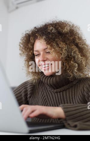 Cheerful young woman typing code on laptop computer at home. Female programmer person coding on notebook pc Stock Photo