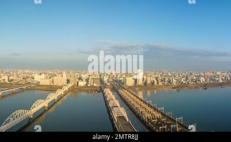 Vehicle bridge next to train bridge over wide river next to city after sunrise Stock Photo