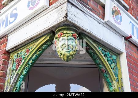 Carved wooden head and face of the green man hanging above the entrance to a public house Stock Photo