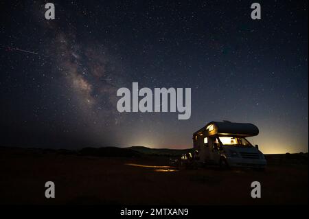 Motorhome RV parked under stars on a pier by the sea, Crete, Greece. Travelers with camper van are resting overnight under milky way on an active fami Stock Photo