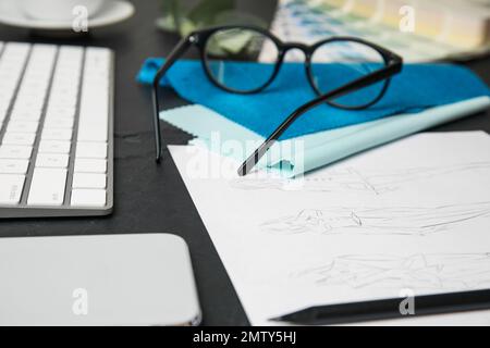 Sketches of clothes, smartphone and keyboard on black stone table, closeup. Designer's workplace Stock Photo