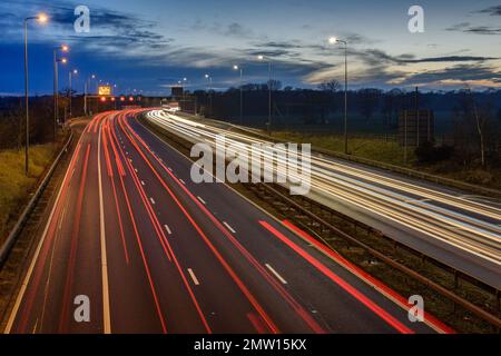 Speeding traffic on M42 motorway during evening rush hour leaves light trails and streaks due to slow shutter speed and long exposure photography. Stock Photo