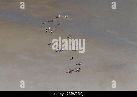 Aerial view over group of tourists walking with guide during guided tour on mudflat / mud flat in summer, Wadden Sea, Schleswig-Holstein, Germany Stock Photo