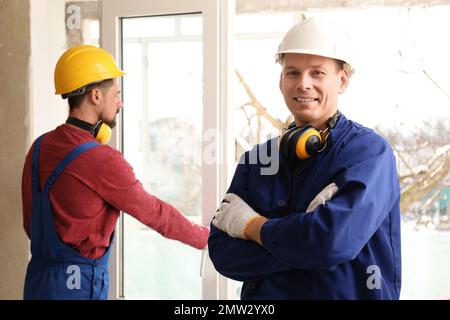 Workers in uniform installing plastic window indoors Stock Photo