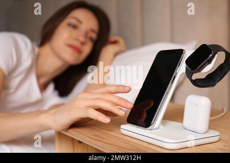 Woman taking smartphone from wireless charger in bedroom Stock Photo