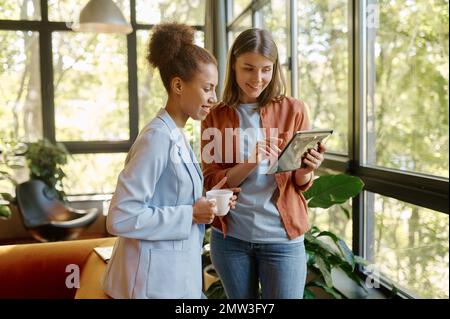 Two young business woman enjoying pleasant conversation in coworking space Stock Photo
