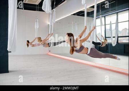 Female group doing fly yoga stretching exercises in fitness training class Stock Photo