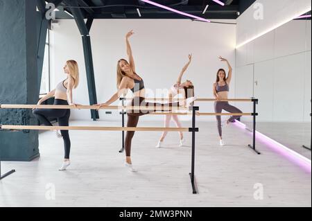 Young women dancers stretching legs, practicing ballet movement at barre Stock Photo