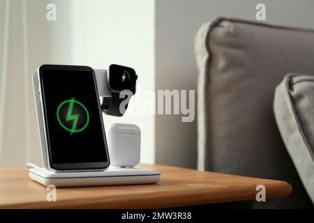 Smartphone, watch and earphones charging on wireless pad in room. Space for text Stock Photo