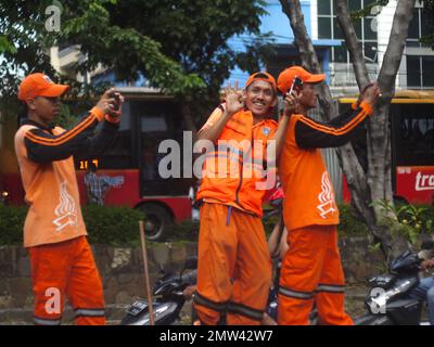 portrait of three men wearing orange shirts and hats. the two people are taking pictures using their cellphones and one other person is smiling. Stock Photo