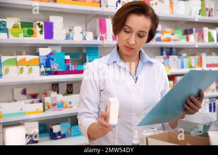 Professional pharmacist with clipboard and medicine in drugstore Stock Photo