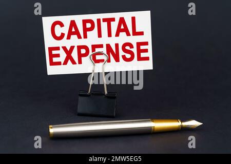 Business concept. On the black surface is a pen, an office paper clip with a business card on which is written - Capital Expense Stock Photo