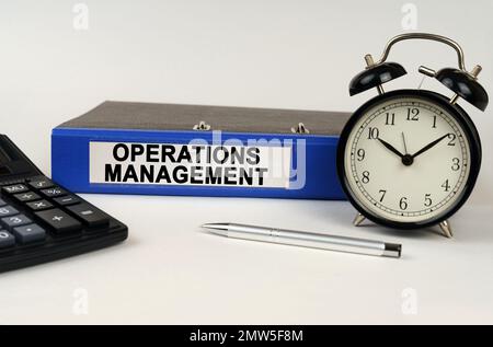 Business concept. On a white surface, an alarm clock calculator and a folder with the inscription - Operations Management Stock Photo