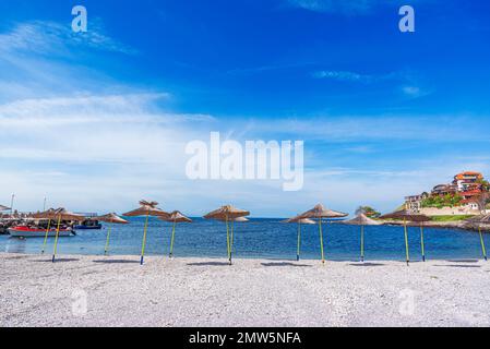 Straw beach umbrellas and sun loungers by the sea. Stock Photo