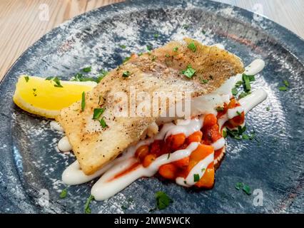 Italian cod fillet on top of chickpeas with seasoning on a dark plate. Stock Photo