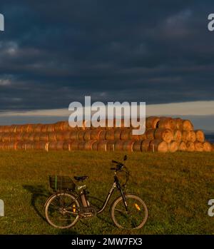 Hay balls and electric bike on field near Ceske Budejovice town in sunrise time in color autumn Stock Photo