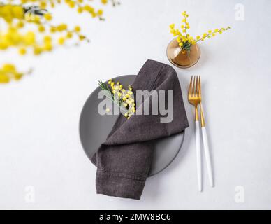 Festive table setting for the spring celebration of women's day, birthday or mother's day with yellow mimosa flowers on a light background. The concep Stock Photo