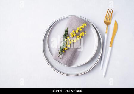 Festive table setting for the spring celebration of women's day, birthday or mother's day with yellow mimosa flowers on a light background. The concep Stock Photo