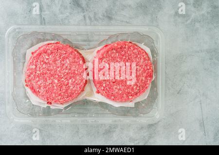 Burger patties in plastic container close-up. Fresh raw burger patties close-up on a grey stone background, copy space Stock Photo