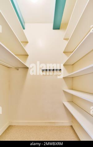 a walk - in closet with white shelvings and shelves on the wall, there is an open door Stock Photo