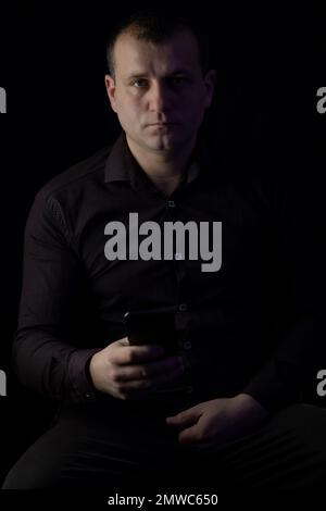 A man with a phone in a shirt on a black background. Stock Photo
