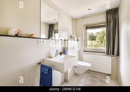 a bathroom with a toilet, sink, and window in the photo is taken to the right there are two towels hanging on the Stock Photo