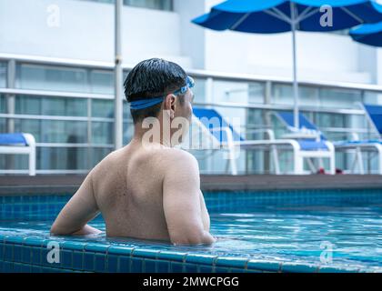 Back view of man in the pool, relaxing by the side. Vacation or travel concept. Stock Photo