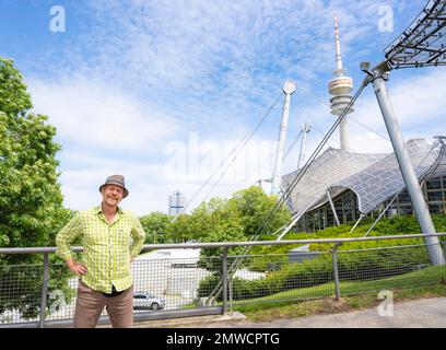 Friendly smiling man at the Olympic tower with Olympic tent roof, BMW tower on the left, Olympic Park, Olympic grounds, Munich, Upper Bavaria Stock Photo