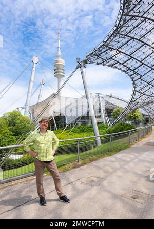 Friendly smiling man at the Olympic tower with Olympic tent roof, Olympic Park, Olympic grounds, Munich, Upper Bavaria, Bavaria, Germany Stock Photo