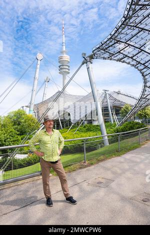 Friendly smiling man at the Olympic tower with Olympic tent roof, Olympic Park, Olympic grounds, Munich, Upper Bavaria, Bavaria, Germany Stock Photo