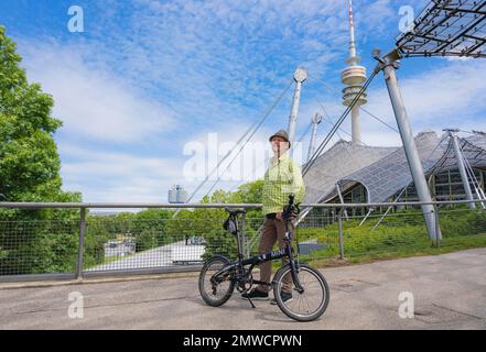 Man with bicycle at the Olympic Tower with Olympic tent roof, BMW Tower on the left, Olympic Park, Olympic Grounds, Munich, Upper Bavaria, Bavaria Stock Photo