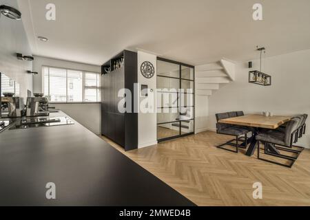 a living room with wood flooring and white walls there is a wooden dining table in front of the wall Stock Photo