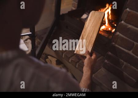 Man putting dry firewood into fireplace at home, closeup. Winter vacation Stock Photo