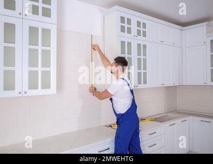 Worker using measuring tape while installing new furniture in kitchen Stock Photo