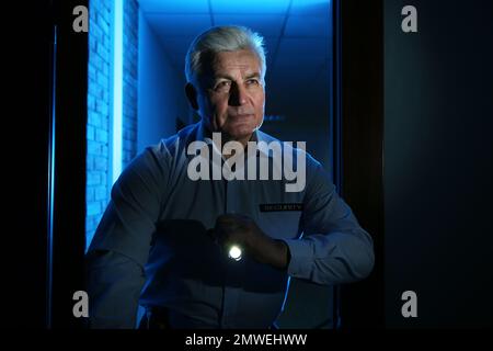 Professional security guard with flashlight checking dark room Stock Photo