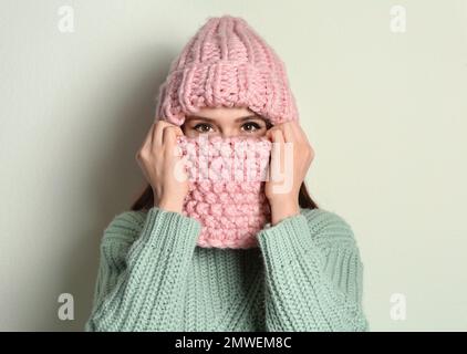 Young woman wearing warm sweater, snood and hat on light background. Winter season Stock Photo