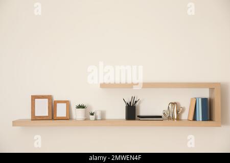 Wooden shelves with books, photo frames and decorative elements on light wall Stock Photo