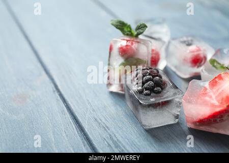 Ice cubes with different berries and mint on blue wooden table, closeup. Space for text Stock Photo