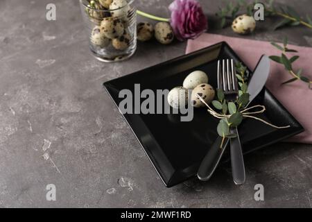 Festive Easter table setting with quail eggs and floral decoration on dark background Stock Photo