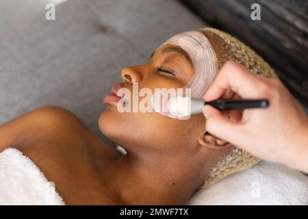 Hand of beautician giving facial to relaxed african american woman with brush Stock Photo